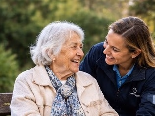 A carer and an older woman laughing together on a garden bench